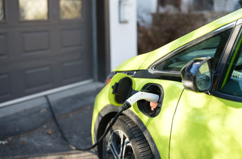 image of a lime green electric vehicle charging in the driveway of a home